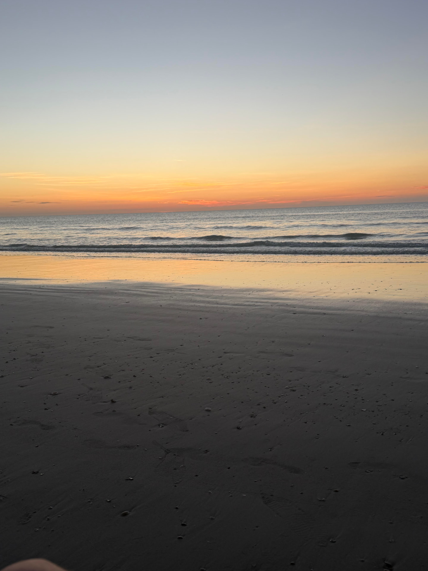 The ocean just before sunrise, sky turning gold over wet sand