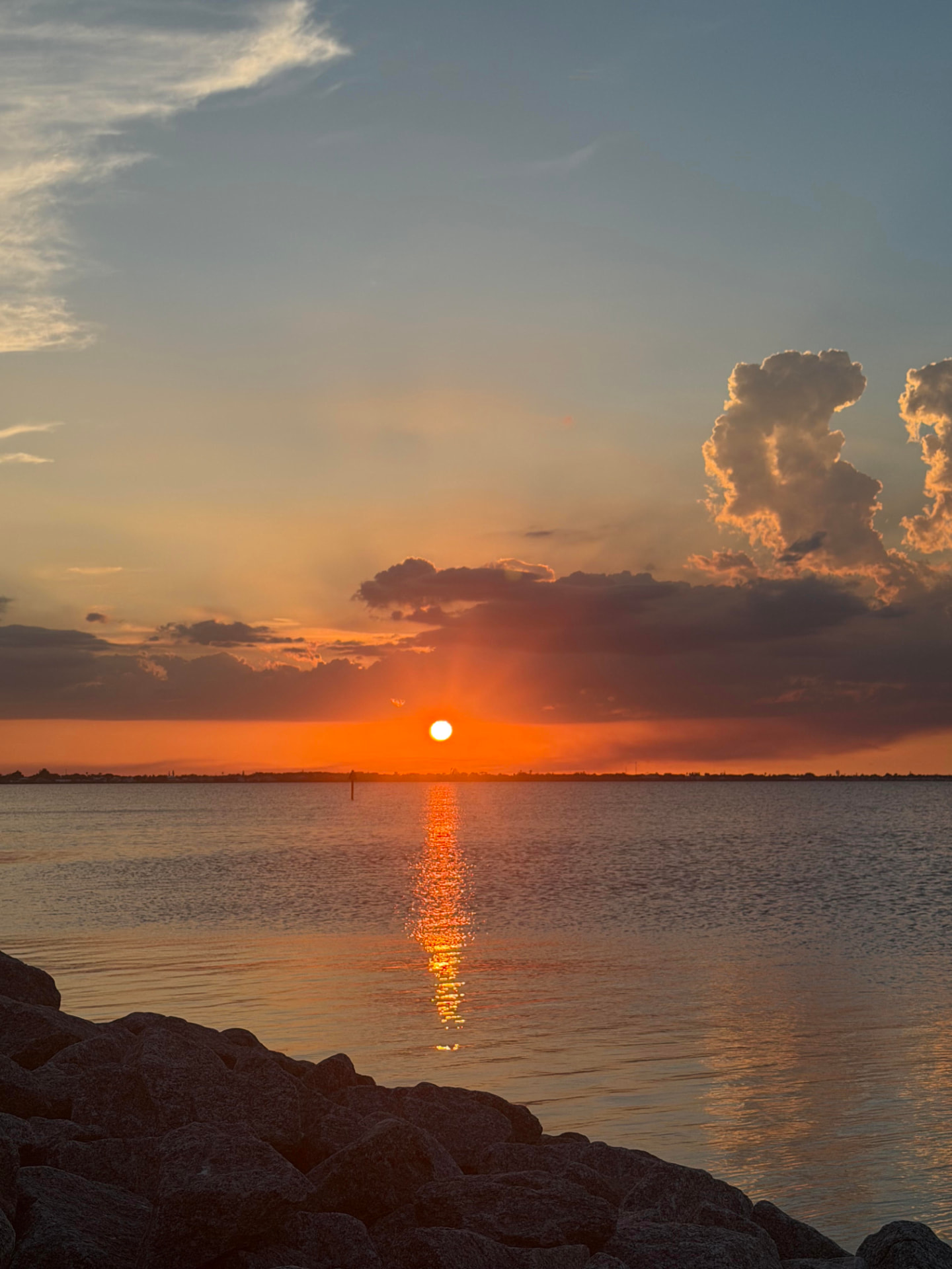 The sun setting low over calm water beyond a rocky shoreline
